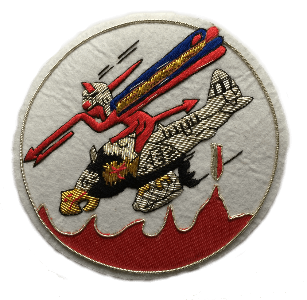 White circle shaped patch. With Red devil character riding on a plane with a bird's head, and holding a red spear. Bomb dropping from under the plane.