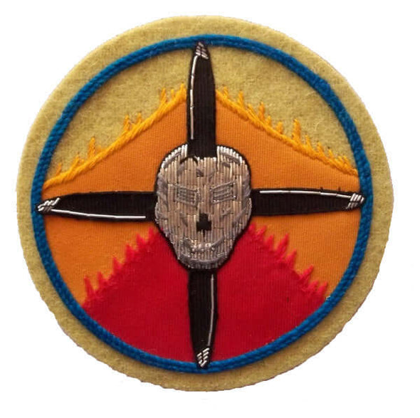 Circle shaped patch with yellow orange red sunrise background. Silver skull in center on crossed black propellers