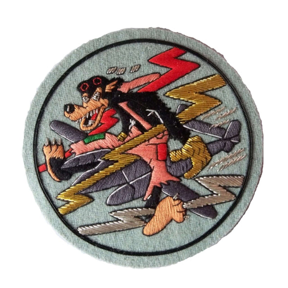 Pale blue circle shaped patch with black wolf character with patched up trousers, sitting on large grey plane flying through lightening bolts