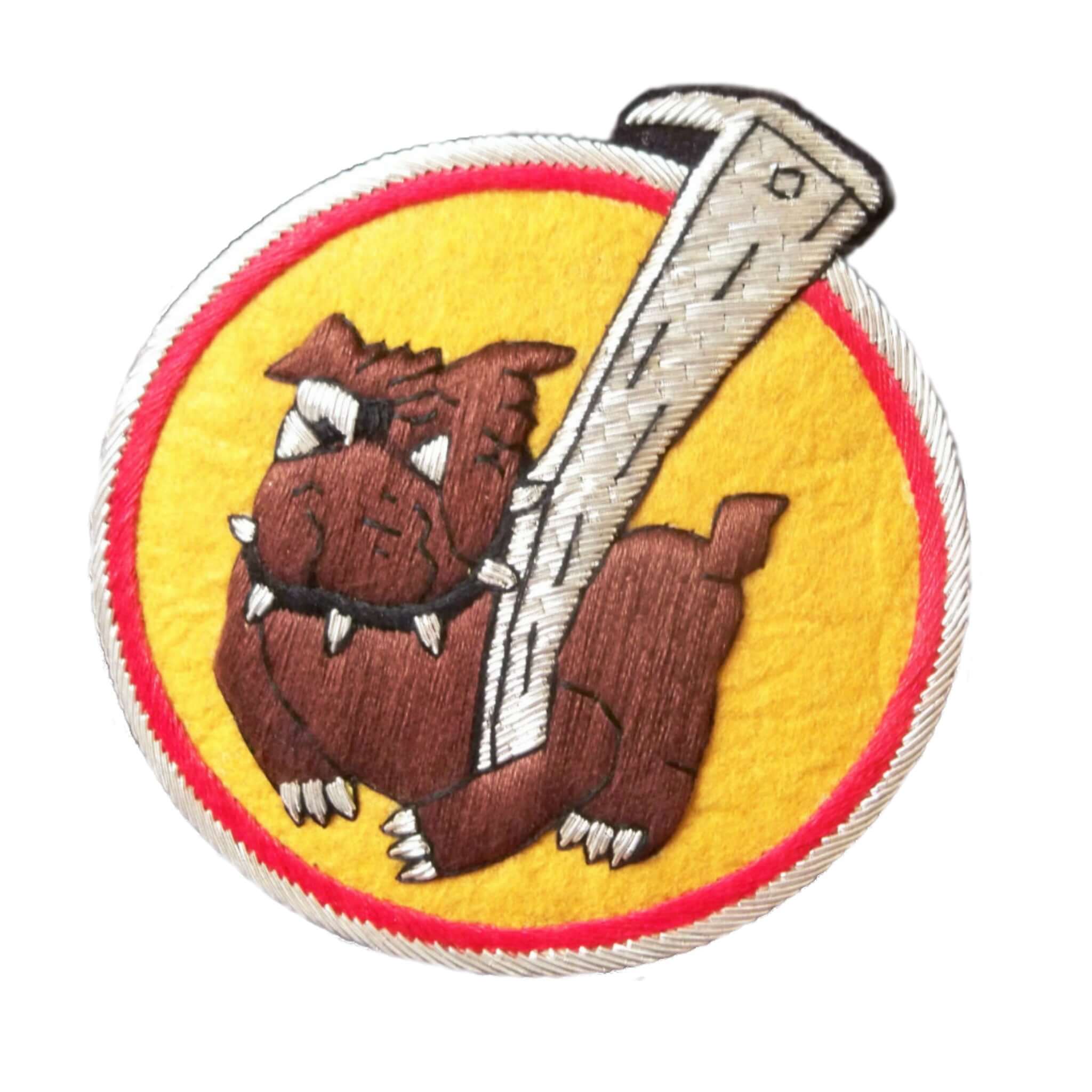 Yellow circle shaped patch with red outer ring. In center is dark brown bulldog holding a large silver stick with left paw