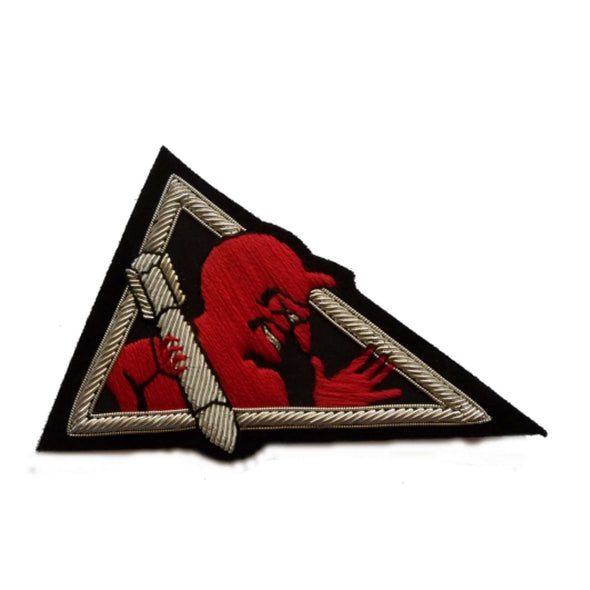 Black triangle shaped patch with silver outer edge. In center is red devil with missile in right hand