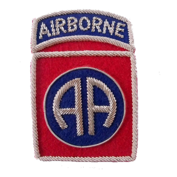 Red rectangle shaped patch with silver outer edge. Center has a blue circle with silver letters 'AA' Top ribbon has word 'Airborne' in silver on dark blue background
