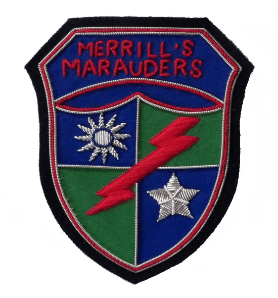 Shield shaped patch with blue and green quarters. Silver sun in top right quarter, silver star in bottom left quarter. Red lightening flash runs top left to bottom right. On top is banner with words, 'Merrill's Marauders'