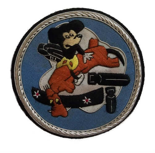 Light blue circle shaped patch with stylized Mickey Mouse sitting astride brown dog and dropping black bomb.