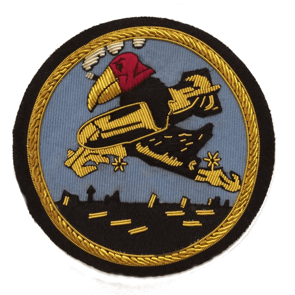 Blue and black circle shaped patch with cigar smoking cartoon eagle flying across rooftops carrying a bomb under his wing