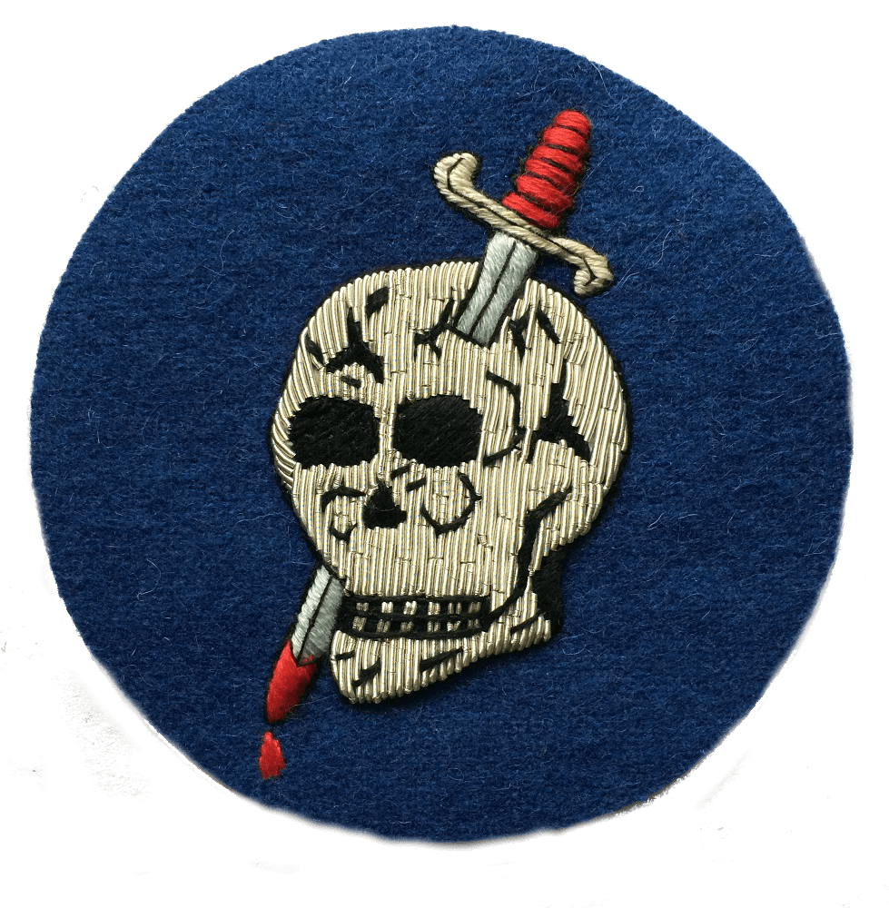 Dark blue circle shaped patch with silver skull in center that has a dagger through the head and blood dripping from tip of dagger blade at bottom of patch