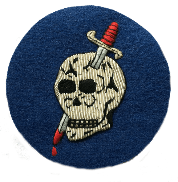 Dark blue circle shaped patch with silver skull in center that has a dagger through the head and blood dripping from tip of dagger blade at bottom of patch