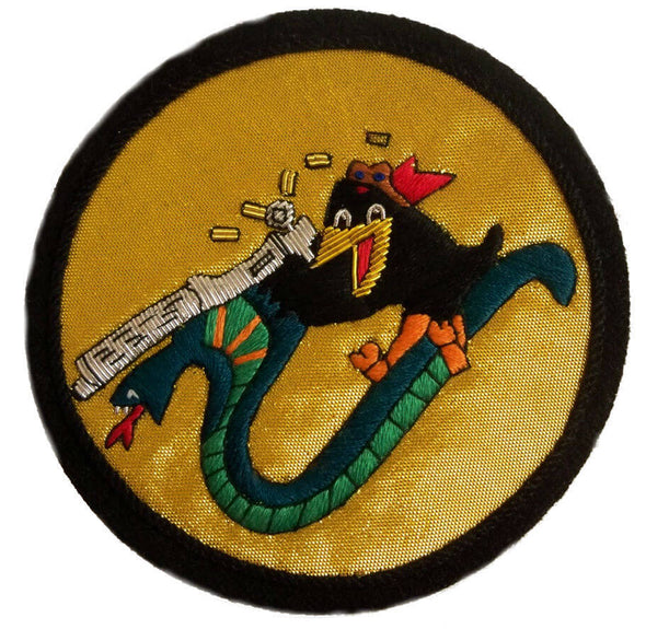 Gold color circle shaped patch with Black smiling bird, sitting on top of a green wiggly snake, firing a silver machine gun
