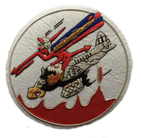White circle shaped patch.  With Red devil character riding on a plane with a bird's head, and holding a red spear.  Bomb dropping from under the plane.