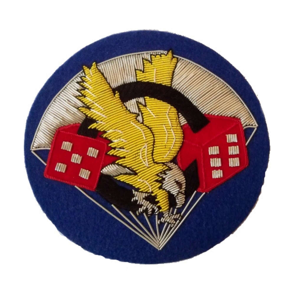 Dark blue color circle shaped patch with Silver parachute in background.  In center are two red dice, one with 5 dots, the other with 6 dots, and a black zero in the center - making the number 506.   A golden eagle is flying through the black zero