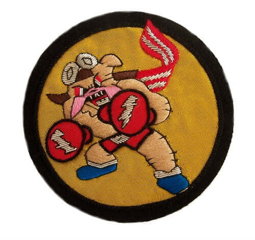 Gold circle shaped patch with black outer ring.  Cartoon Bulldog character in center, snarling and in a boxing stance,  wearing red boxing gloves, blue boots and a red/white striped scarf.  He wears flying goggles on his head.