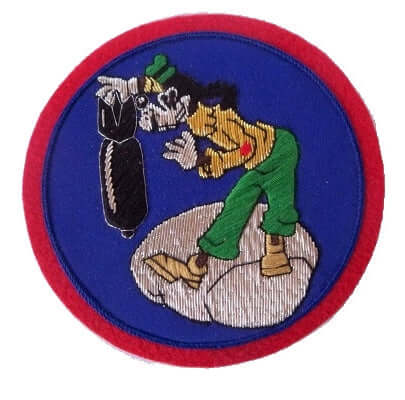 Dark blue circle shaped patch with red outer ring.  In center is 'Goofy' style cartoon character, standing on a silver cloud and dropping a black missile