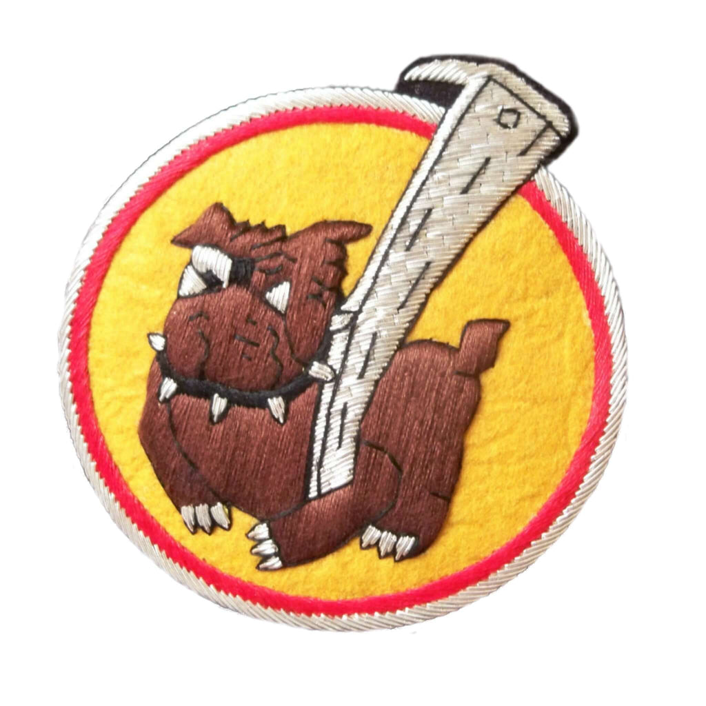 Yellow circle shaped patch with red outer ring.  In center is dark brown bulldog holding a large silver stick with left paw