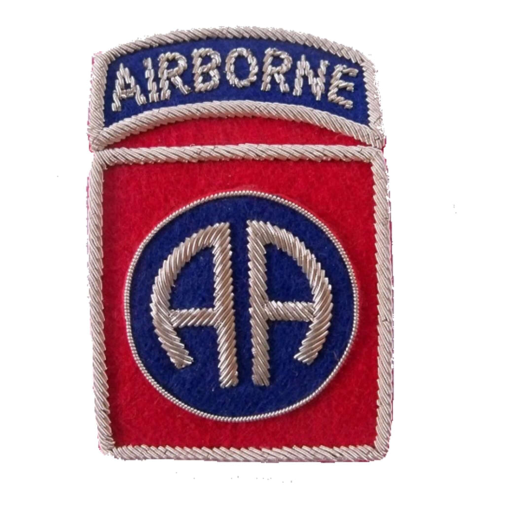 Red rectangle shaped patch with silver outer edge.  Center has a blue circle with silver letters 'AA'   Top ribbon has word 'Airborne' in silver on dark blue background