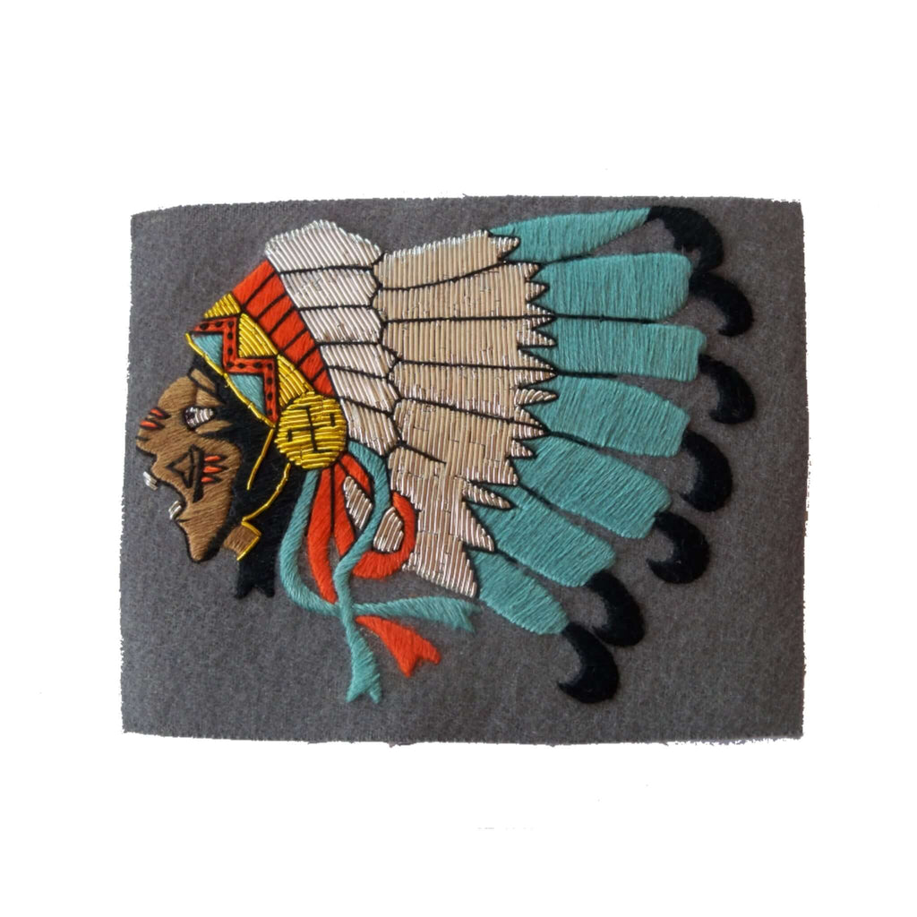 Grey rectangle shaped patch with Native Indian Chief head, facing right, in full headress of white, blue, black feathers.